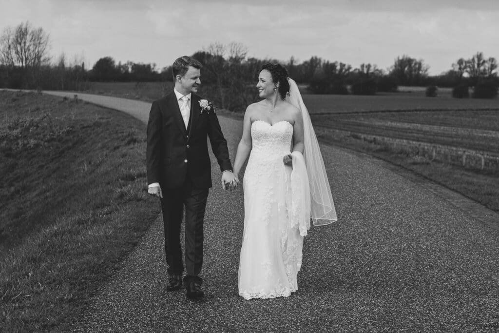 Bruidspaar komt aanlopen op de dijk tijdens fotoshoot van bruiloft
