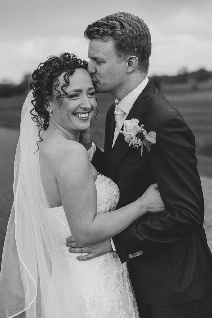 De bruidegom geeft de bruid een kus tijdens fotoshoot.